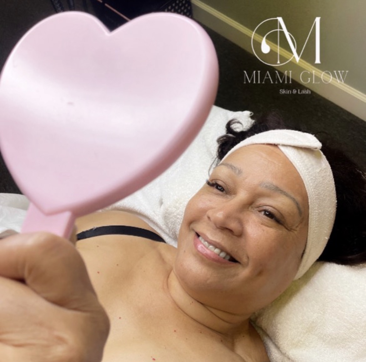A client smiling at her new lashes with a pink heart mirror