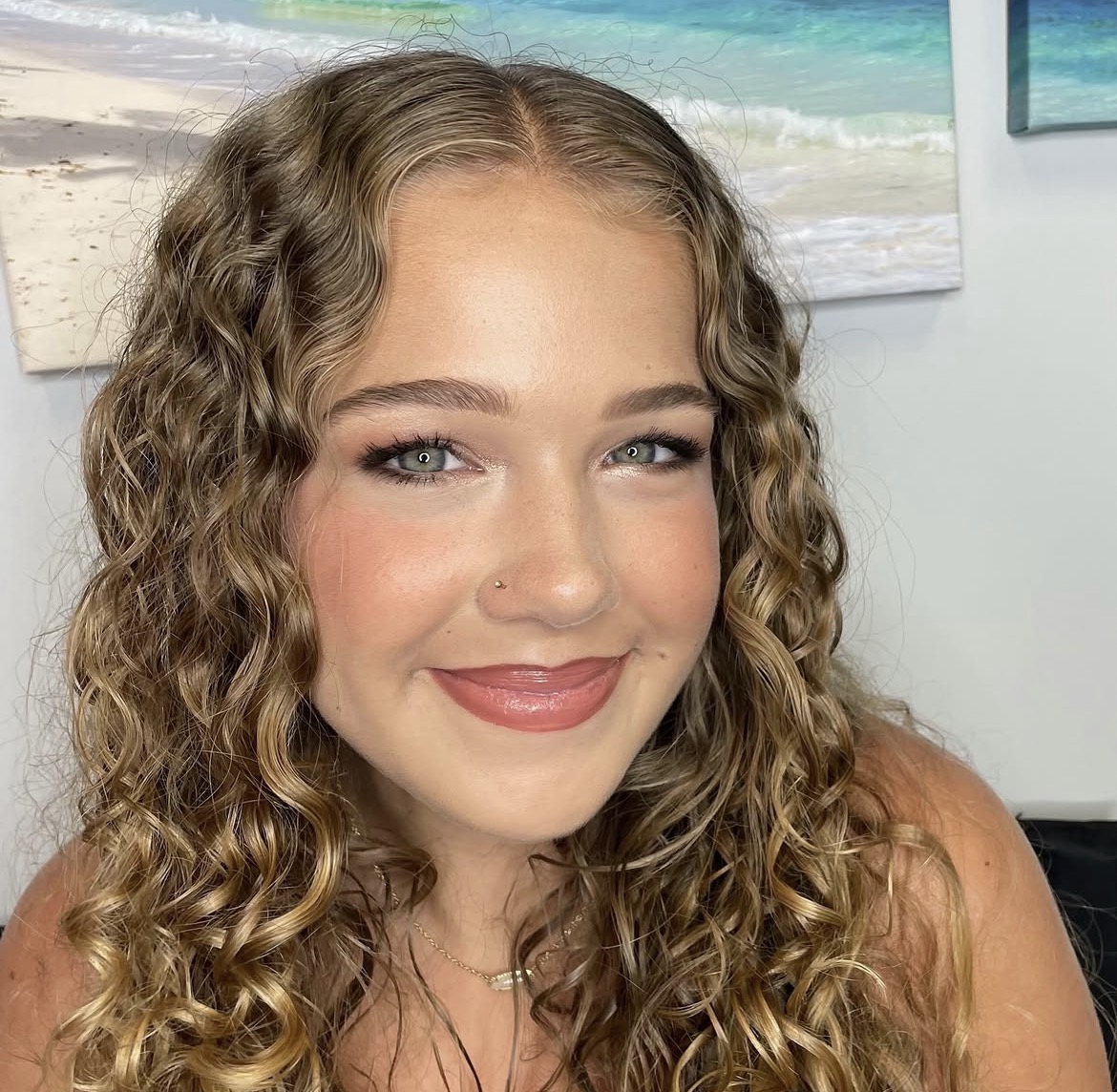 A client with soft curls and fresh lash extensions smiling in our studio